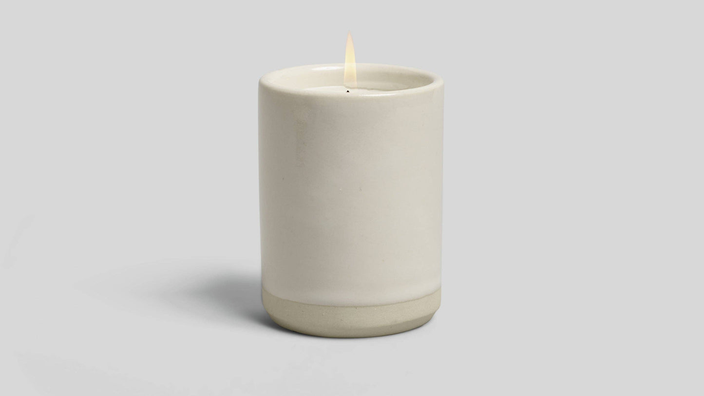 Ceramic candle holder with a lit candle on a light gray background