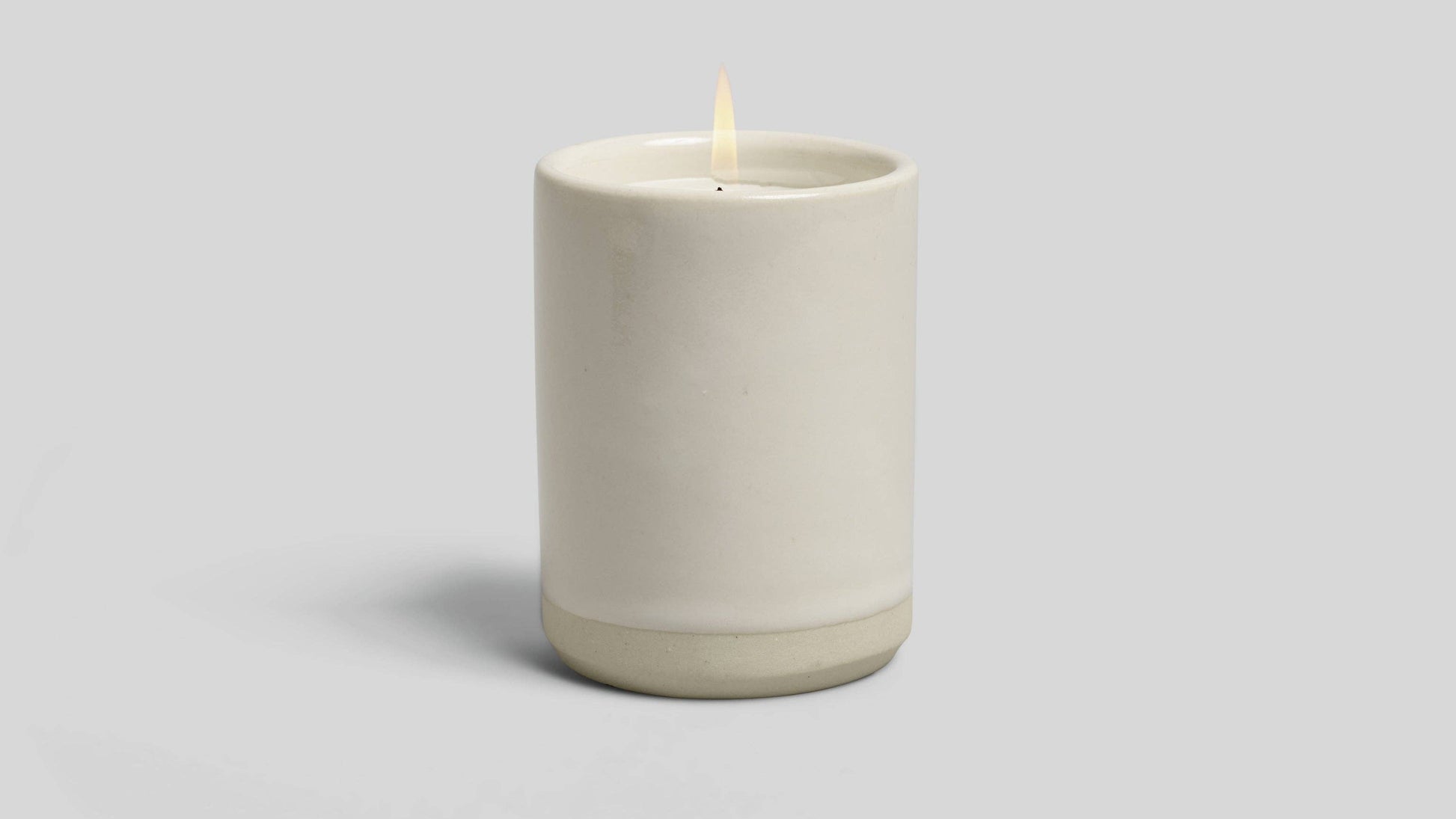 Ceramic candle holder with a lit candle on a light gray background