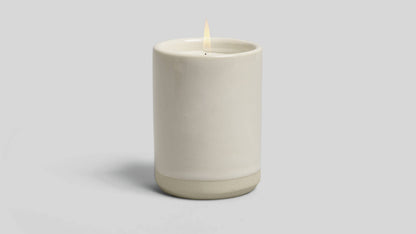 Ceramic candle holder with a lit candle on a light gray background