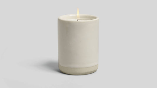 Ceramic candle holder with a lit candle on a light gray background