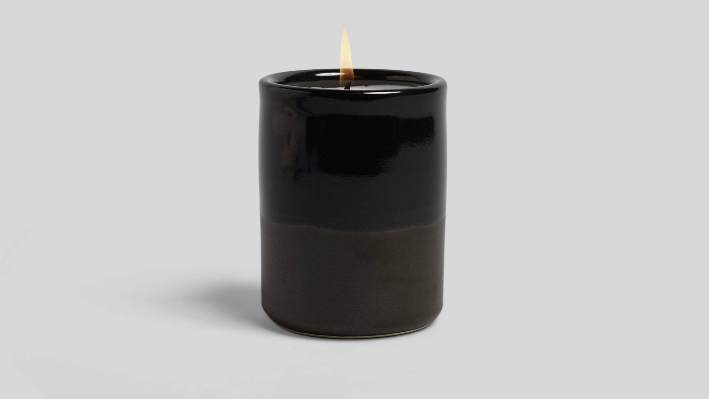 Black candle with a lit wick on a light gray background