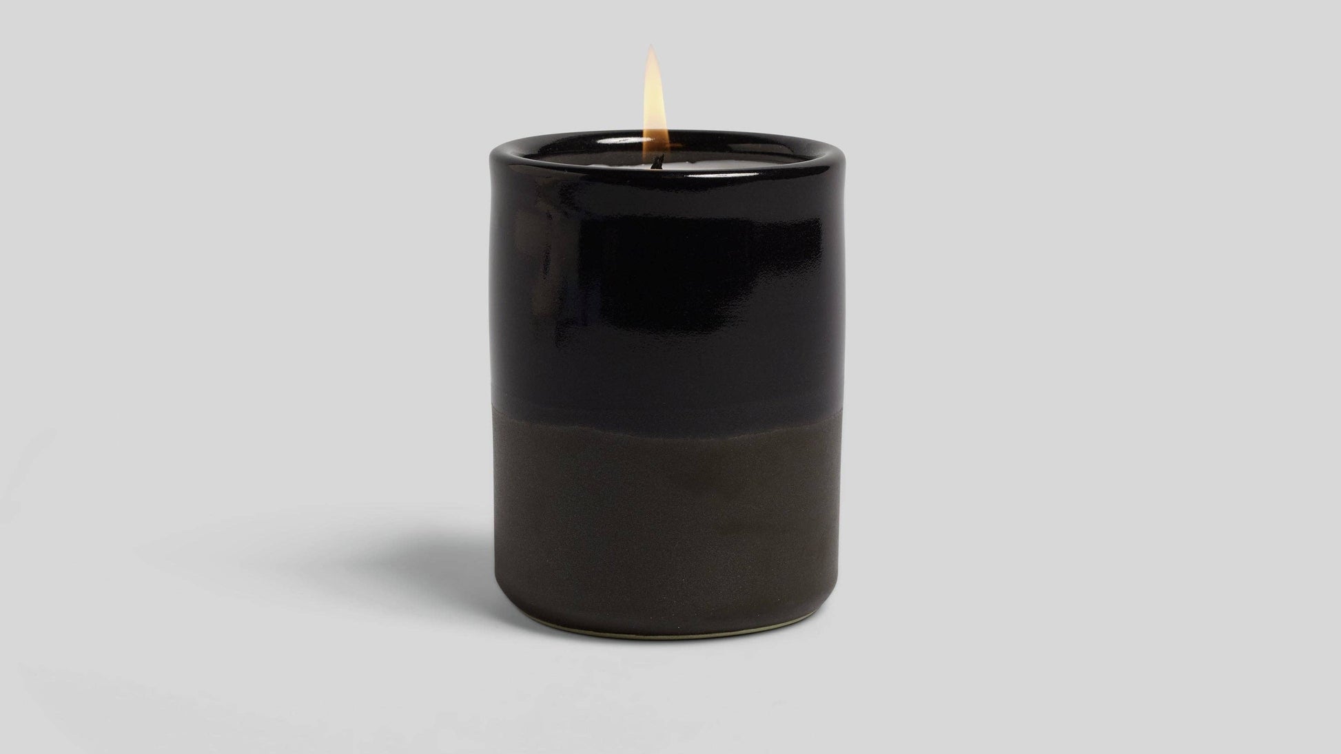 Black candle with a lit wick on a light gray background