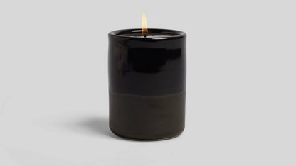 Black candle with a lit wick on a light gray background