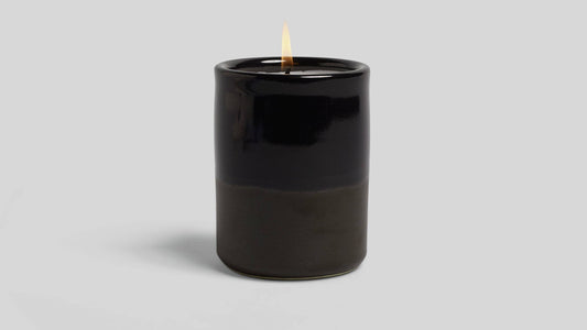 Black candle with a lit wick on a light gray background